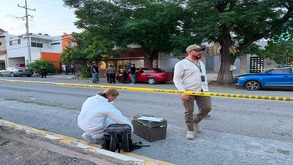 Se observa a un hombre y una mujer en la calle, una mujer vestida con traje blanco de perito y una cinta amarilla de precaución.