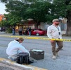 Se observa a un hombre y una mujer en la calle, una mujer vestida con traje blanco de perito y una cinta amarilla de precaución.