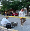 Se observa a un hombre y una mujer en la calle, una mujer vestida con traje blanco de perito y una cinta amarilla de precaución.