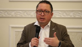 Hombre de lentes y cara gorda hablando ante un micrófono.