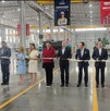 Se observa a mujeres y hombres de pie sosteniendo un listón rojo.