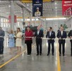 Se observa a mujeres y hombres de pie sosteniendo un listón rojo.
