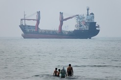 Varias personas se ven en aguas poco profundas mientras un carguero parece fondeado más lejos en el estrecho de Ormuz, cerca de Bandar Abbas, Irán,