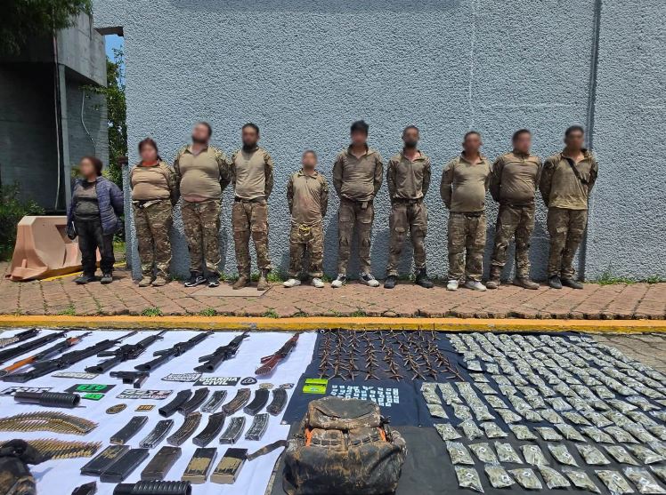 Grupo de hombre y mujeres, entre ellos menores de edad, con los rostros censurados parados delante de armas y drogas en el suelo