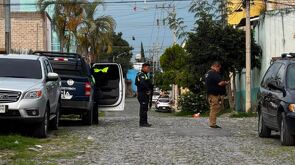Policía de Jalisco con un arma larga en medio de la calle con una patrulla y un elemento de Ciencias Forenses a los lados