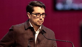Hombre de lentes y peinado hacia atrás hablando ante un micrófono.