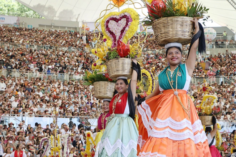 Mujeres danzando en la Guelaguetza sujetando una canasta sobre la cabeza.