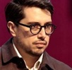 Hombre de lentes y peinado hacia atrás hablando ante un micrófono.