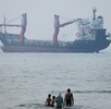 Varias personas se meten en el agua en la orilla mientras un carguero aparece fondeado en el estrecho de Ormuz, ante la costa de Bandar Abbas, Irán