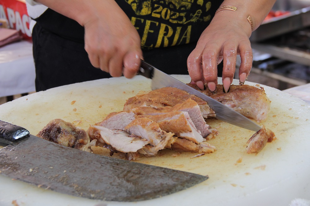 Mujer cortando carnitas con un cuchillo.