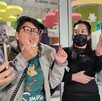 Se observa a dos mujeres, una con lentes y otra cargando un celular en la mano donde se ve un perrito color blanco.