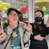 Se observa a dos mujeres, una con lentes y otra cargando un celular en la mano donde se ve un perrito color blanco.
