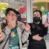 Se observa a dos mujeres, una con lentes y otra cargando un celular en la mano donde se ve un perrito color blanco.