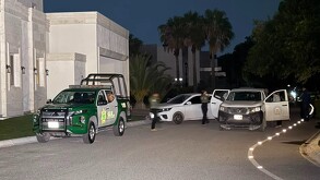 Se observa a varias personas caminando en la vía pública, es de noche.