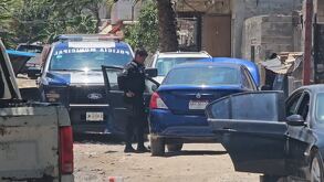 Patrulla de la Policía de Zapopan dentro de un área acordonada con autos estacionados detrás en un camino de tierra