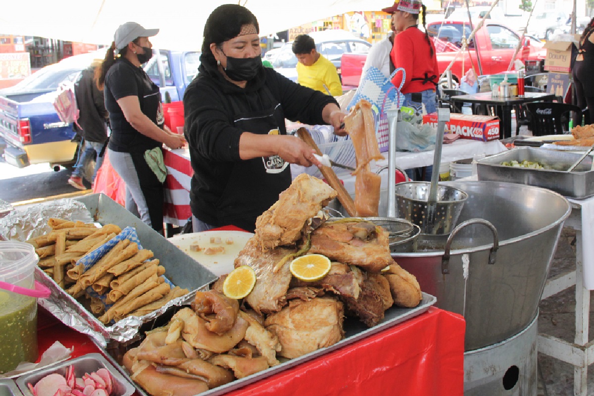 Mujer atendiendo en un puesto de comida mientras saca carnitas de un cazo.