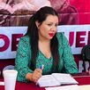 Mujer de vestido verde platicando con una persona en una mesa de diálogo.