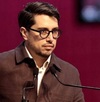 Hombre de lentes y peinado hacia atrás hablando ante un micrófono.