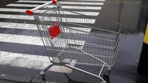 Carrito metálico de supermercado en medio de un estacionamiento con el suelo mojado por lluvia, un cruce peatonal y un poste