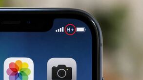 Símbolo de H+ entre el ícono de la batería y barras de señal en la esquina de la pantalla de un teléfono Iphone con íconos de cámara y galería debajo
