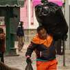 Un hombre recolector de basura con un uniforme naranja cargando una bolsa negra grande de basura