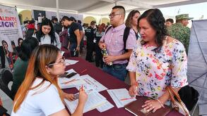 una mujer y un hombre frente a una mesa donde recultadores en una feria de empleo en puebla