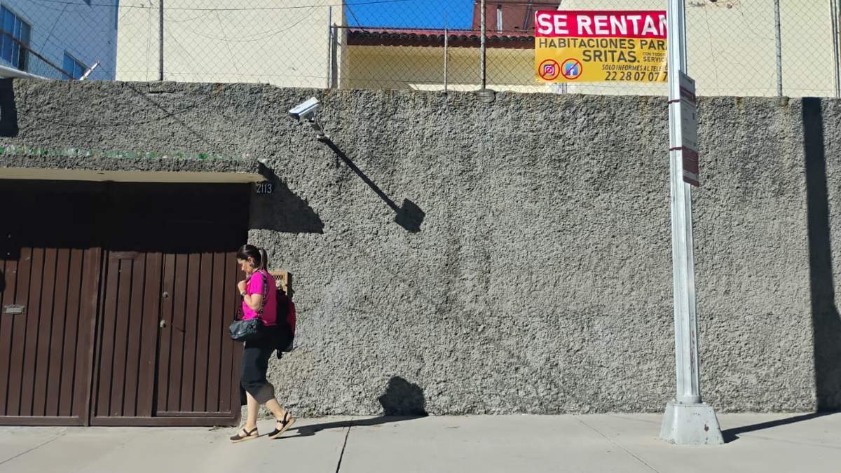 una mujer caminando por la calle y la fachada de una casa con un anuncio de habitación en renta en puebla