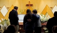 Personas abrazadas frente al ataúd de una persona muerta.