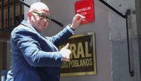 Hombre colocando una placa roja afuera de un restaurante en Puebla.
