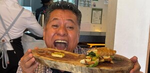 Hombre mordiendo un plato de comida y mirando hacia la cámara.
