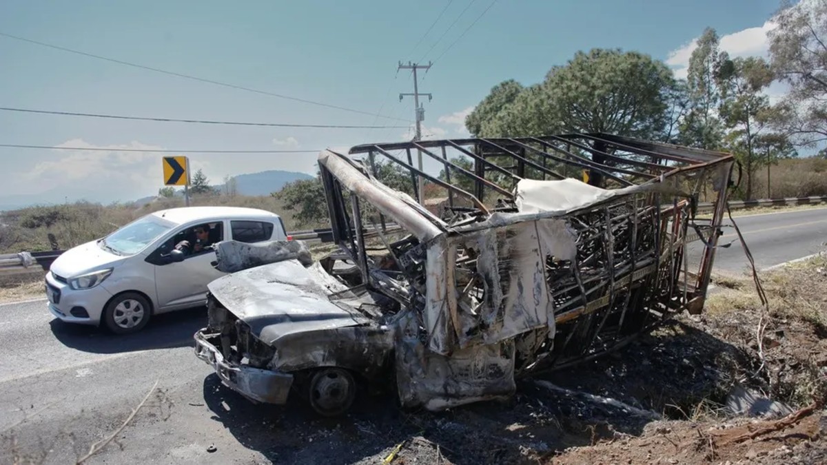 Camioneta de carga quemada en medos de una carretera de Jalisco con un auto pasando al lado durante captura de El Mencho