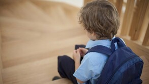 Un niño visto de espaldas con una mochila puesta y sentado en unas escaleras de madera