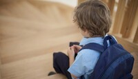 Un niño visto de espaldas con una mochila puesta y sentado en unas escaleras de madera