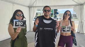 dos mujeres y un hombre muestran su playera y número para participar en la carrera multimedios