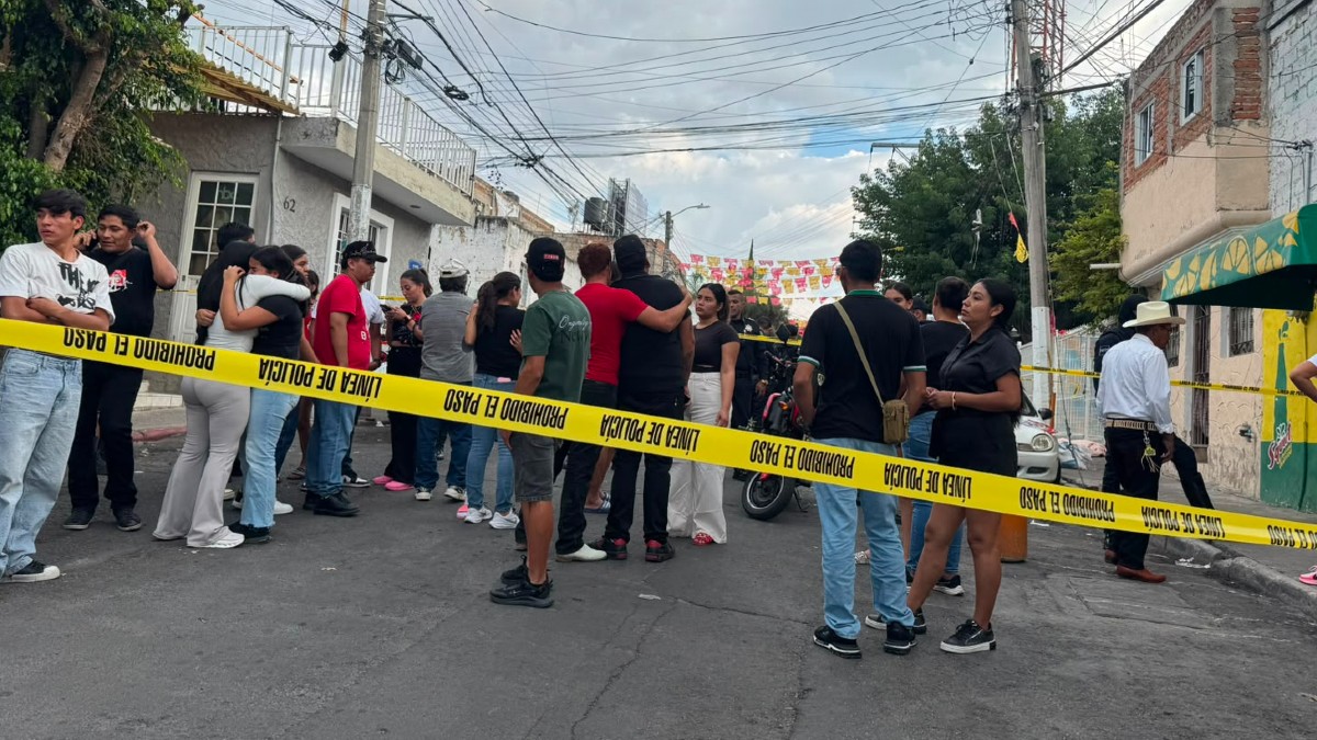 Multitud de personas reunidas detrás de un área acordonada por la policía en calles de Zapopan con casas y autos alrededor
