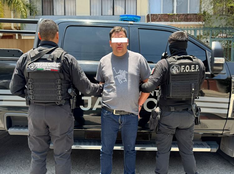 Hombre colombiano con los ojos censurados por un recuadro blanco siendo detenido por dos policías de Jalisco frente a una patrulla