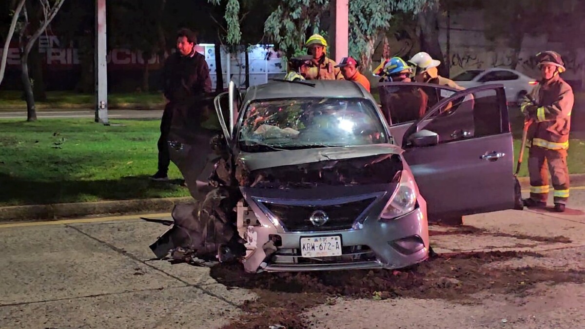 Auto Nissan color gris destruido del costado derecho, con las puertas abiertas y con oficiales de Protección Civil y Bomberos alrededor