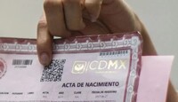 Persona sosteniendo la esquina de un acta de nacimiento de la Ciudad de México color rojo con un código QR