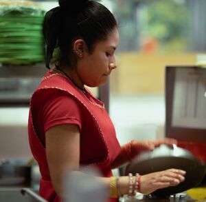 Una mujer joven con un delantal rojo vista de perfil en una cocina
