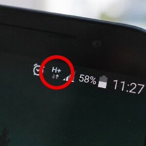 Vista de la esquina de una pantalla de un teléfono celular con el símbolo H+ encerrado en un círculo rojo en medio de símbolos de alarma y batería