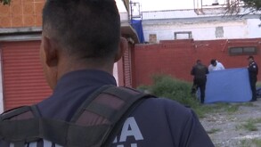Se observa a un policía de espalda y unas personas al fondo sosteniendo una manta azul.