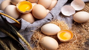 Canasta con huevos blanquillos con dos de ellos rotos y con la yema expuesta extendidos en una mesa con paja