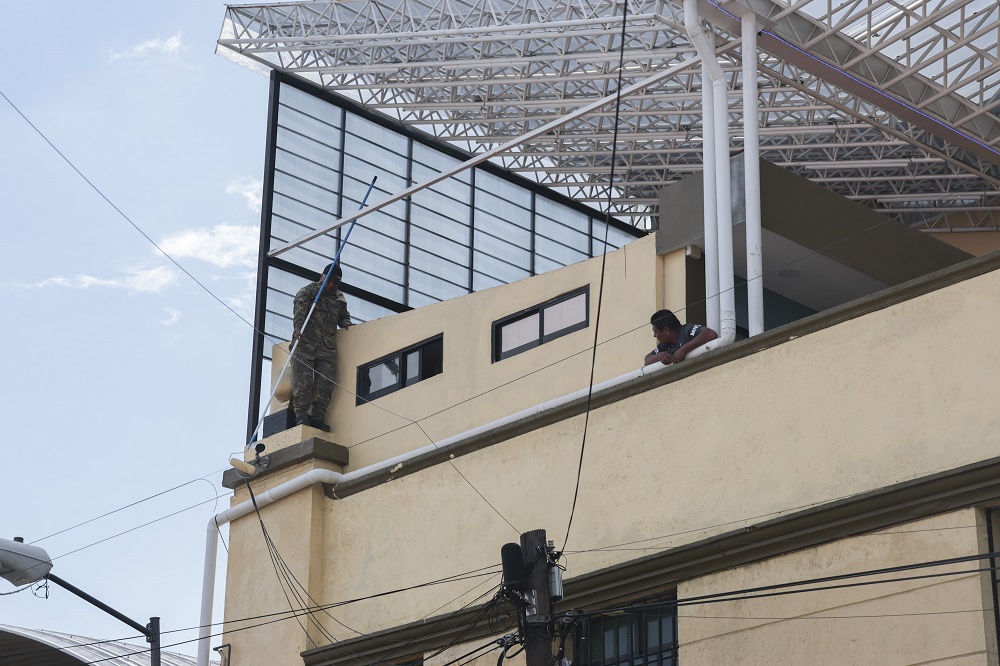 Hombre con ropa militar montado en una escalera para pintar una pared.