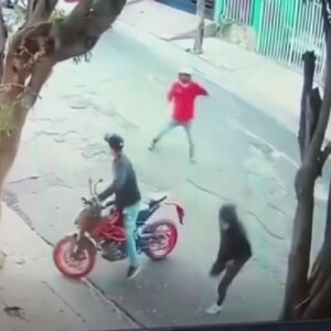 Captura de pantalla de un video de seguridad que muestra a dos presuntos asaltantes tratando de robar la moto de un hombre en medio de la calle