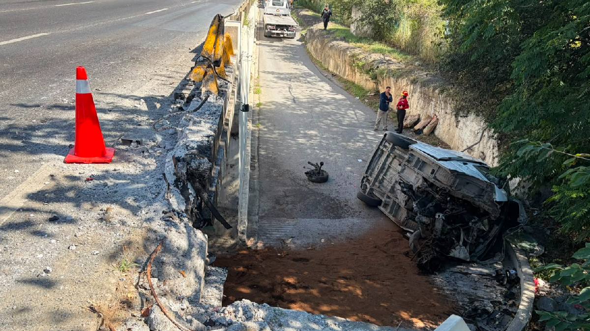 Cuerpos de emergencia laboran en la zona donde la unidad volcada quedó sobre uno de sus costados tras precipitarse desde la vía.