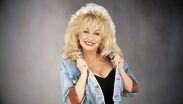 Dolly Parton posando con una de sus características sonrisas y vistiendo uno de sus célebres vestuarios | Pinterest