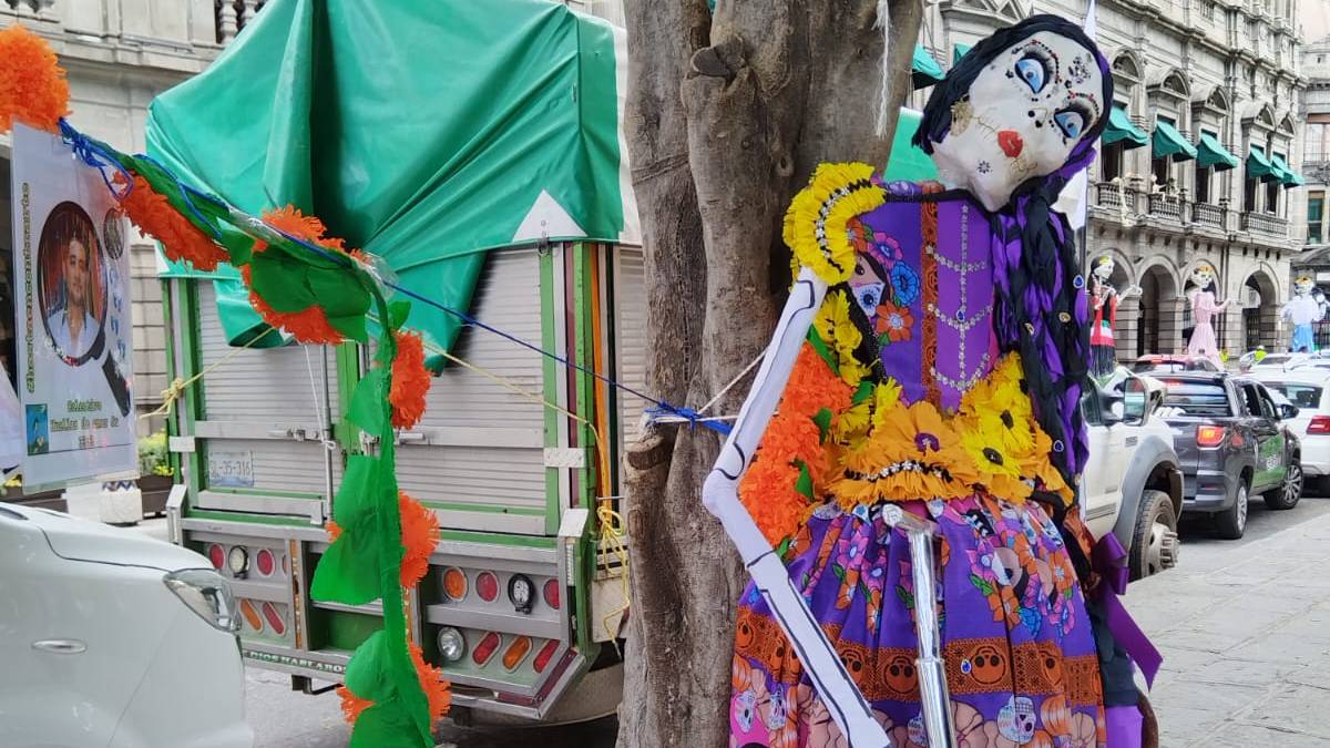 La "Catrina Inconforme" porta un atuendo morado alusivo al Día de Muertos y sostiene un pico y una pala |