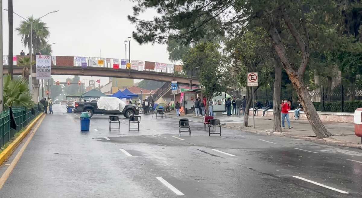 Casas de campaña y vehículos permanecen sobre la vialidad como parte del campamento estudiantil instalado frente al plantel.